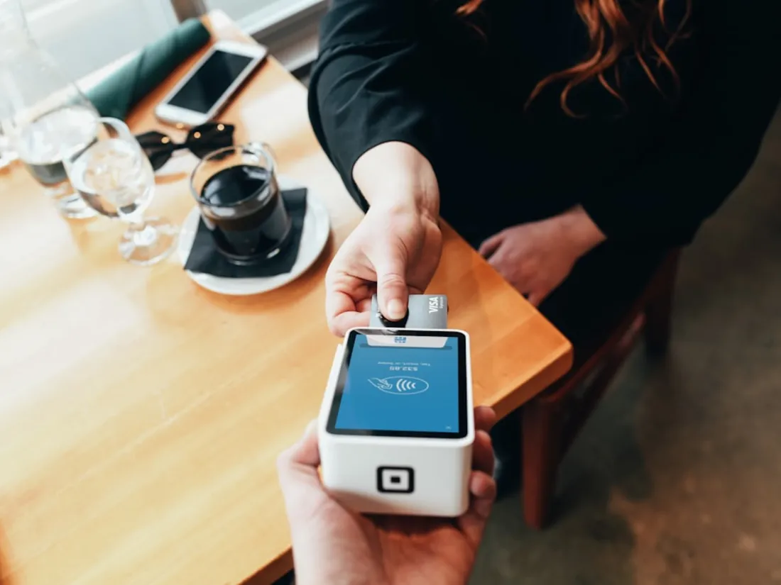 Obsluha účtuje platbu kartou na mobilním platebním terminálu u stolu v kavárně