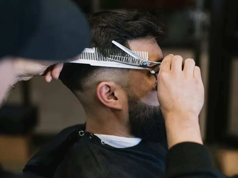 Holič stříhá zákazníkovi vlasy nůžkami v barbershopu